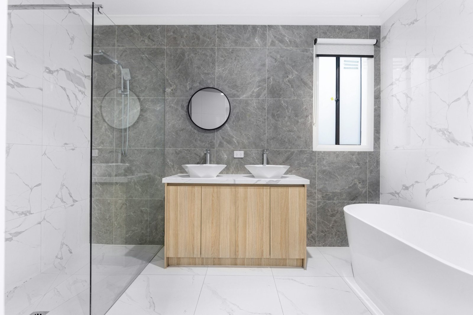 A sleek and stylish modern bathroom with minimalist design, featuring dual washbasins, marble tiles, and a glass shower enclosure.